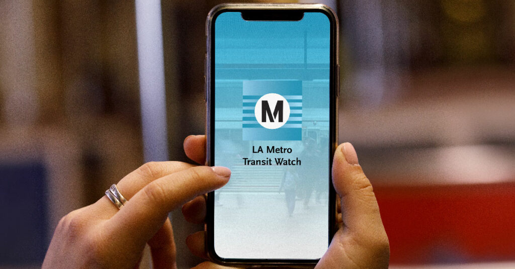 Hands holding a mobile phone using the LA Metro Transit Watch app.