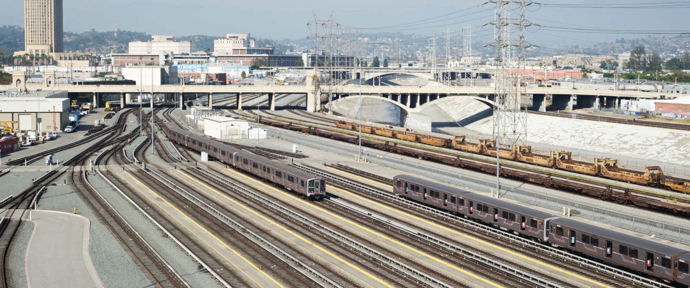 View of Division 20 Portal Widening & Turnback Facility Project tracks, vehicles with LA River and city in background.