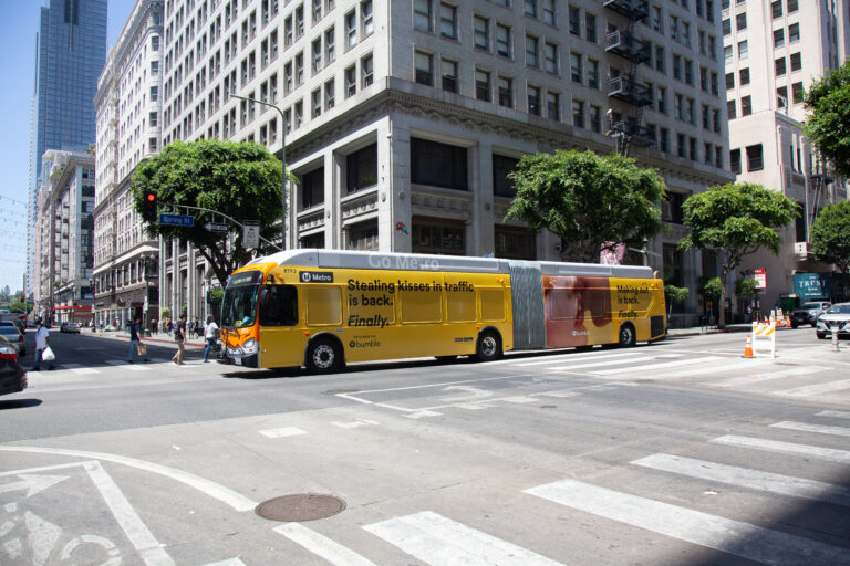 Metro Articulated Bus with bright yellow full advertising wrap passing through intersection in Downtown Los Angeles.