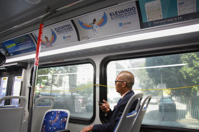 Passenger holding a phone on bus with interior cards along the top of the bus.