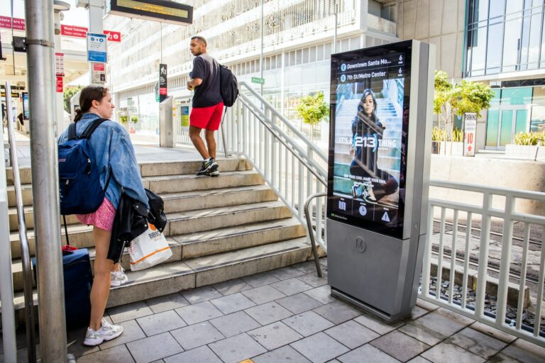 Passengers climbing stairs to platform at station entrance with Los Angeles Digital IxNTouch Kiosk.