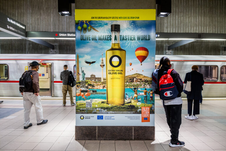 Metro Rail car with passengers in foreground with one resting against a Station Domination Ad for Olive Oil.