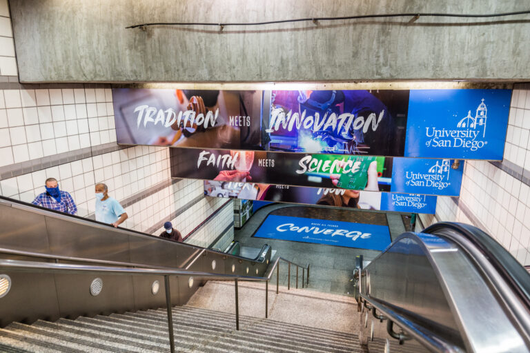 Passengers exiting the Metro Center Station on the escalators with station ads on panels and floor.